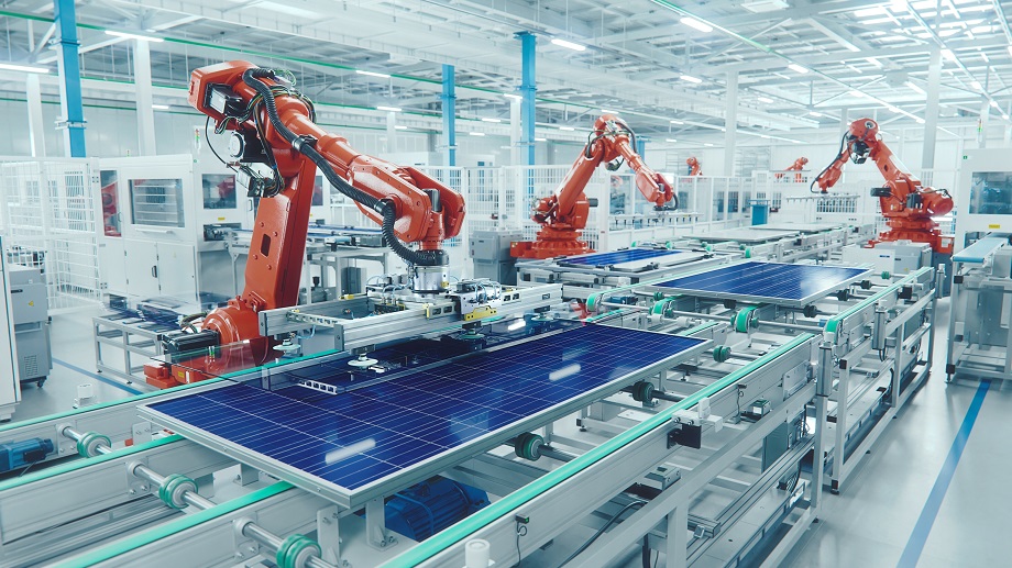 Orange Industrial Robot Arm at Production Line at Modern Bright Factory. Solar Panels are being Assembled on Conveyor. Automated Manufacturing Facility
